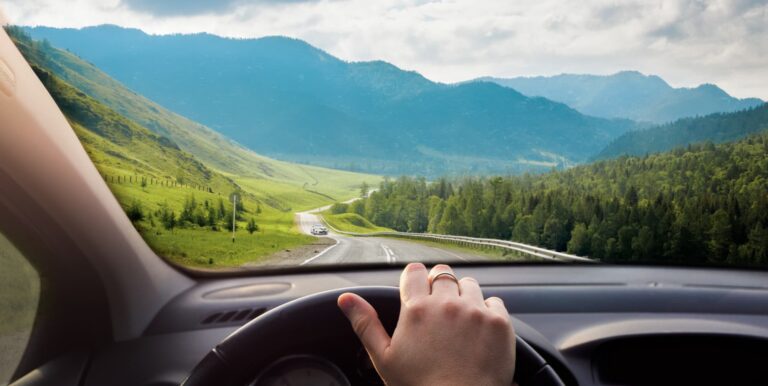 Blick durch die Windschutzscheibe am Tag: kurvige Bergstrasse, entgegenkommendes Auto, klare Sicht